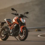 Moto KTM Duke orange sur route sinueuse de montagne, vue de trois-quarts avant, lumière dorée naturelle